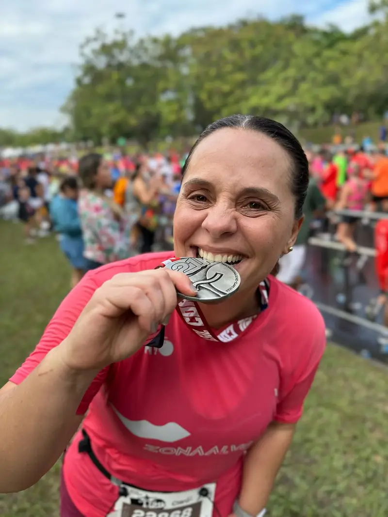 Corredora com camiseta rosa mordendo a medalha após a prova